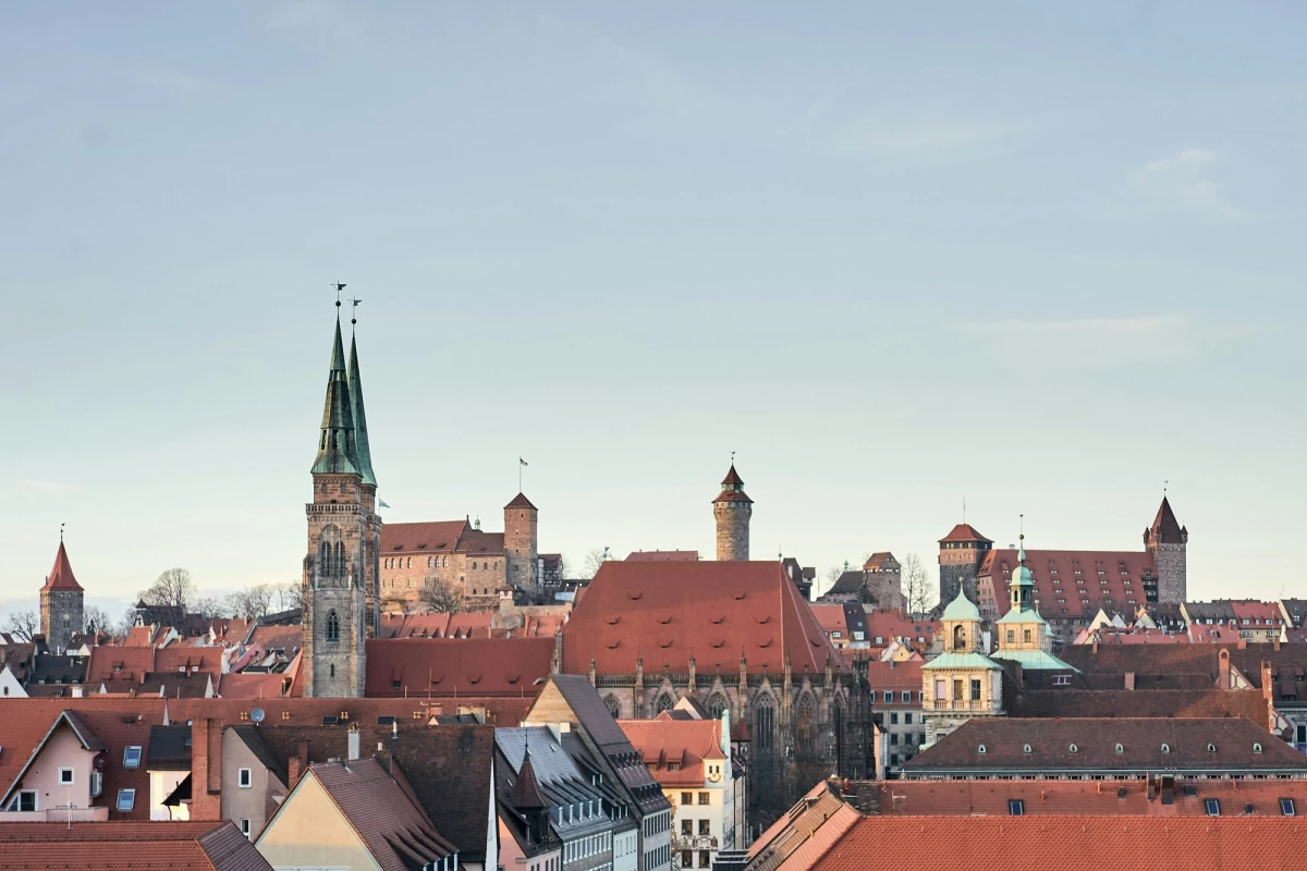 Historische Stadtsilhouette von Nürnberg mit mittelalterlichen Türmen, Kirchen und dicht aneinander gebauten roten Ziegeldächern. Blick über die Altstadt mit charakteristischer Architektur und markanten Gebäuden vor einem klaren Himmel.