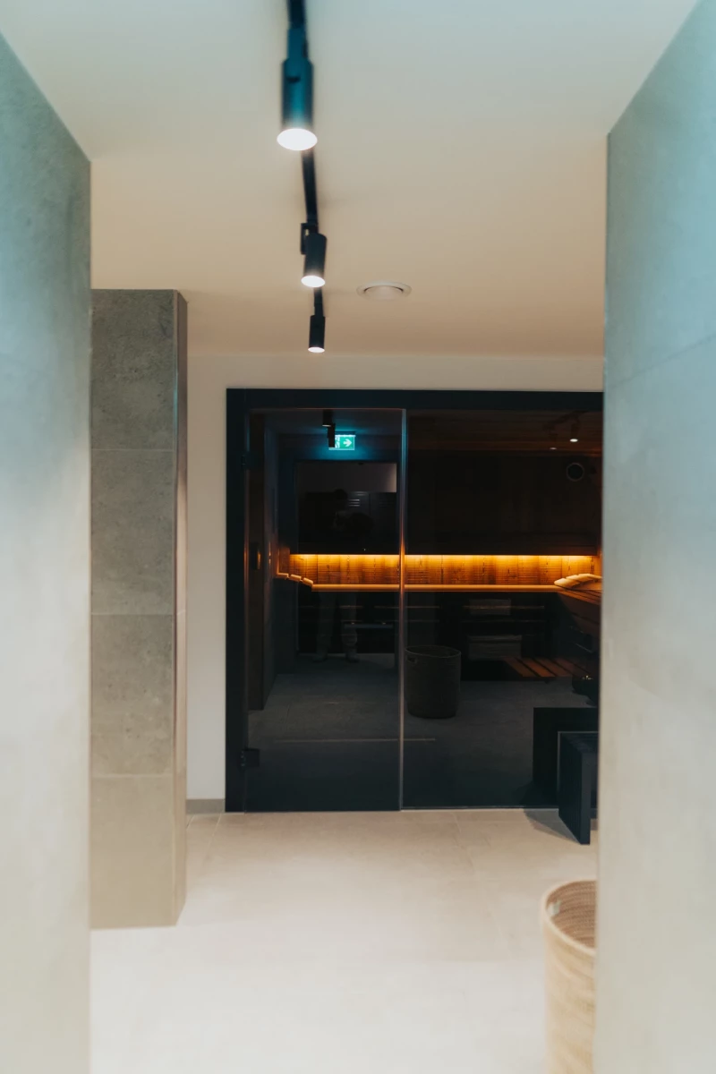 Moderner, minimalistischer Flurbereich mit weißen Wänden und schwarzer Glasfront. Eine beleuchtete bernsteinfarbene Leiste akzentuiert den Raum, während Deckenspots einen dezenten Lichtakzent setzen.