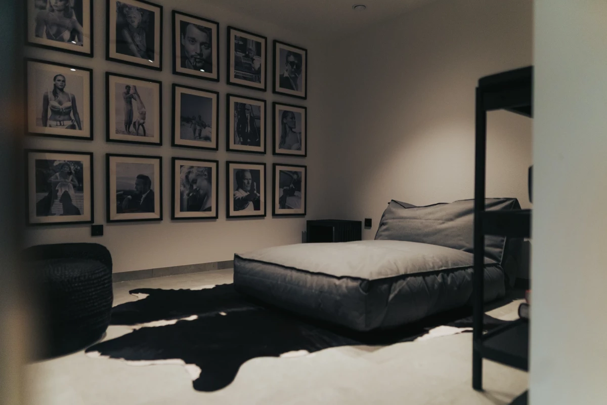Minimalistisches Schlafzimmer mit einer Wand voller schwarzer Fototafeln und einem zentralen Bett mit schwarzer Bettwäsche, das auf einem unregelmäßigen Tierfell-Teppich steht.