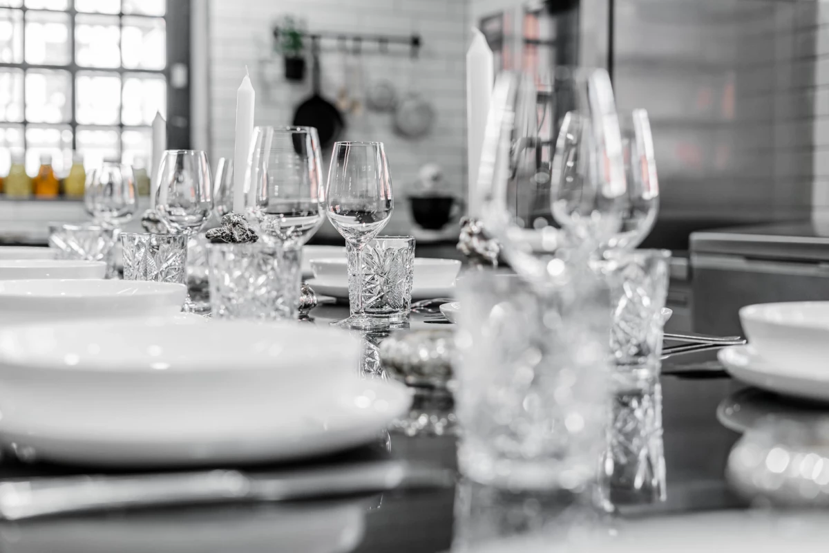 Gedeckter Tisch mit eleganten Weingläsern und Tellern in schwarz-weißer Aufnahme. Detaillierte Tischdekoration in einer modernen Küche oder Bar mit strukturiertem Hintergrund.