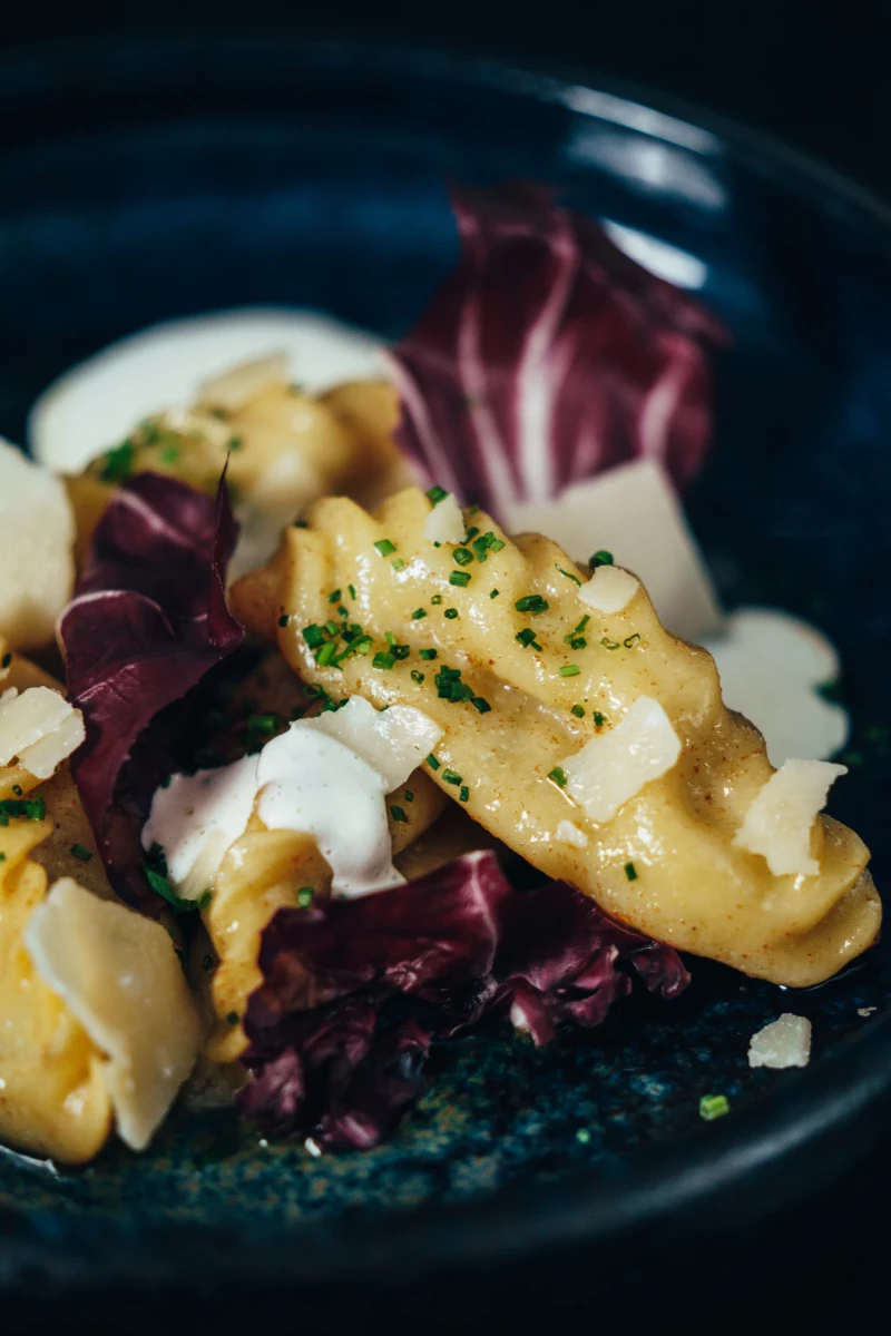 Kartoffelgnocchi mit cremigem Käsesauce, bestreut mit gehackter Petersilie, serviert auf dunklem Teller mit violetten Radicchio-Blättern und bröckeligen Käsestücken.