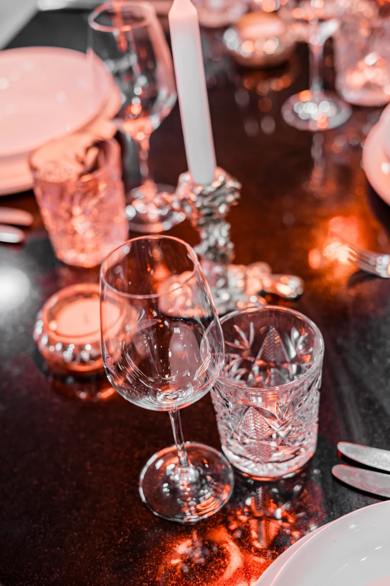 Elegante Bar-Tischszene mit geschliffenen Kristallgläsern, einem Weinglas und einem Whiskyglas. Warmes Licht und glänzende Oberflächen schaffen eine gedämpfte, luxuriöse Atmosphäre mit rötlichen Reflexen.