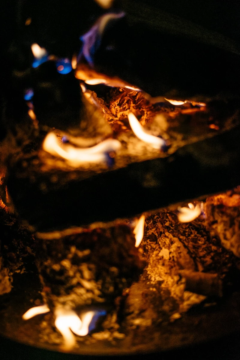 Loderndes Lagerfeuer mit blauen und gelben Flammen, die über dunkle Holzscheite tanzen. Warme, flackernde Lichter erhellen die Dunkelheit mit einer gemütlichen, wärmenden Atmosphäre.