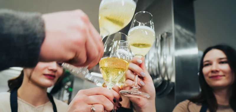 Mehrere Hände stoßen mit Champagnergläsern an. Die Gläser sind gefüllt mit gelblichem Champagner und werden vor einem unscharfen Hintergrund gehoben.