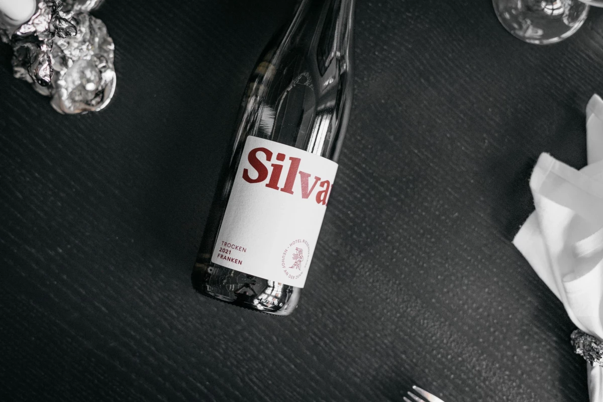 Schwarzweiße Aufnahme einer Flasche Silva mit rotem Logo auf dunklem, strukturiertem Untergrund. Neben der Flasche sind verschwommen Kristalle oder Eisformen und ein weißes Tuch zu erkennen.