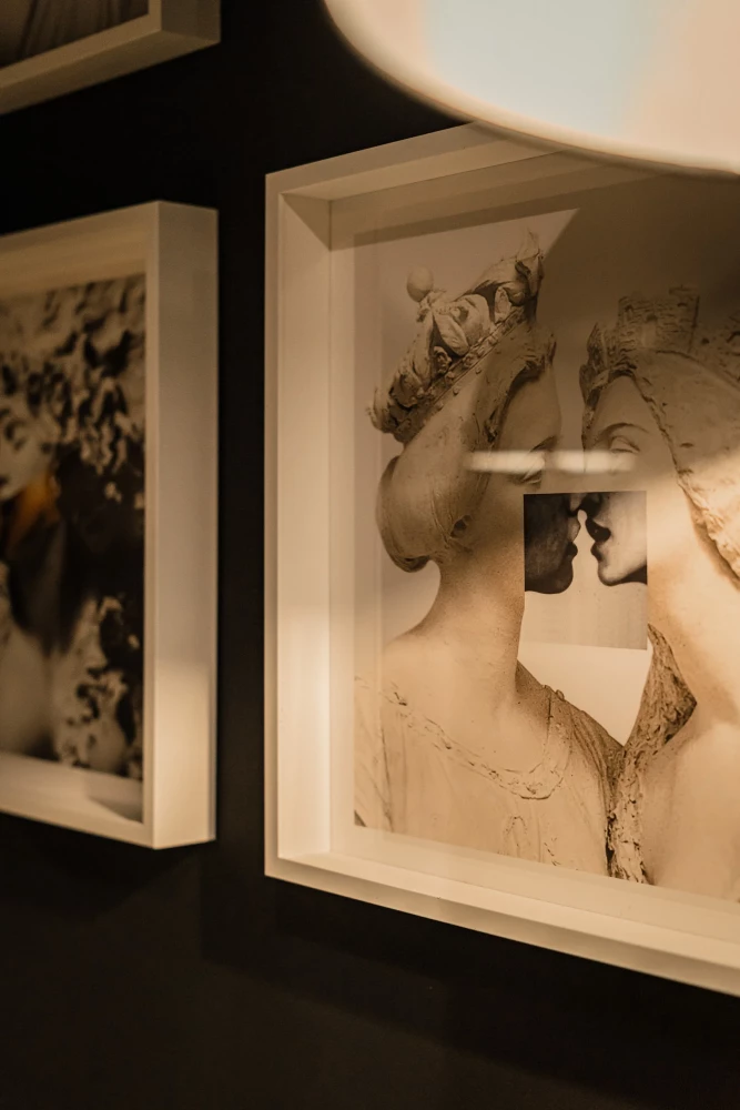 Vintage Schwarzweißfotografie in einem weißen Rahmen, die eine zärtliche Umarmung und einen Kuss zweier Silhouetten zeigt, aufgehängt an einer dunklen Wand neben einem weiteren gerahmten Bild.
