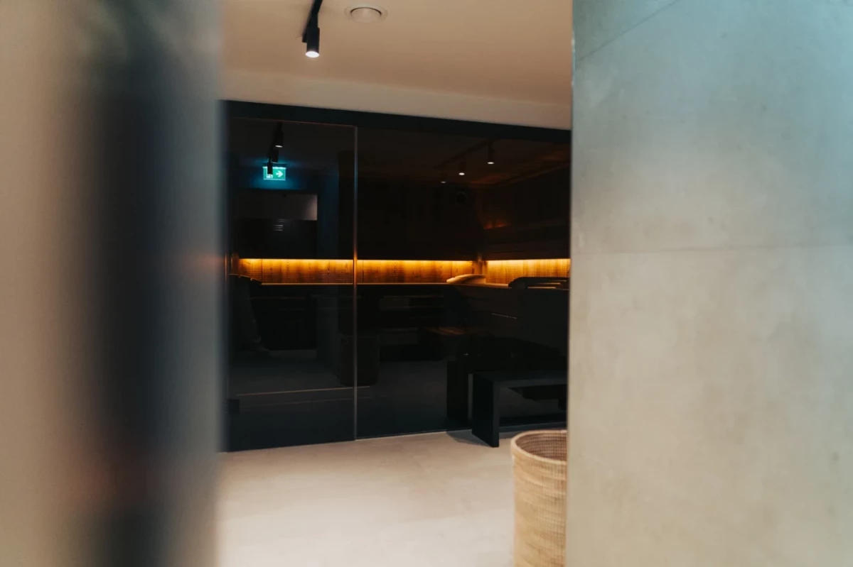 Blick durch eine verschwommene Kante auf eine dunkle Saunalandschaft mit warmgelbem Lichtband und minimalistischem, modernem Interieur.